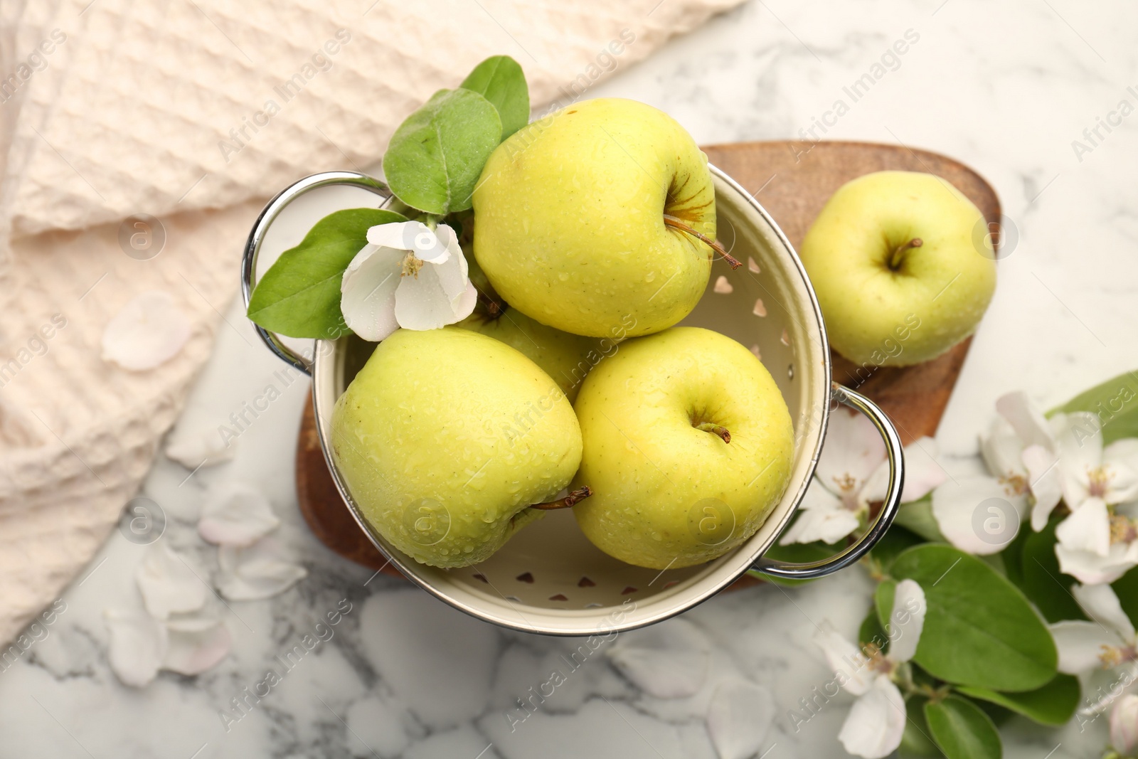 Photo of Colander with fresh apples and beautiful spring blossoms on white marble table, flat lay