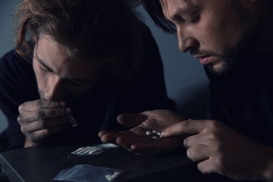 Young addicted men taking drugs on grey background