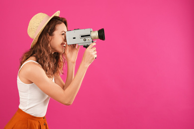 Beautiful young woman using vintage video camera on crimson background, space for text