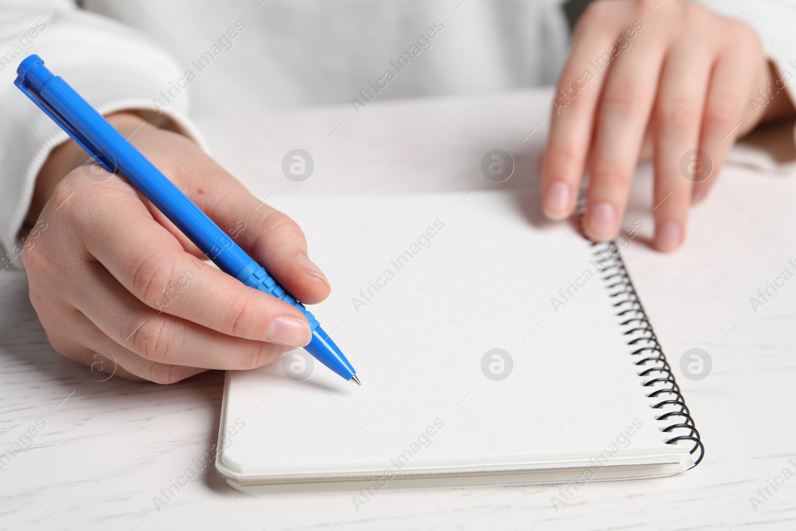 Photo of Woman writing in notebook with pen at white wooden table, closeup