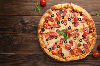 Photo of Tasty pizza with dry smoked sausages, tomatoes, olives, pepper and parsley on wooden table, top view. Space for text