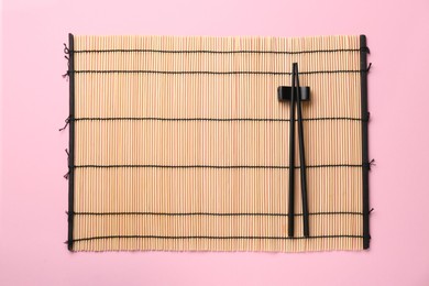 Bamboo mat with pair of black chopsticks and rest on pink background, top view