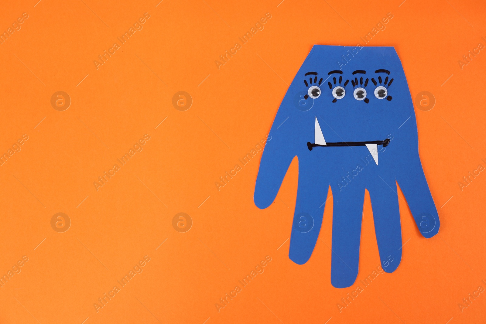 Photo of Funny blue hand shaped monster on orange background, top view with space for text. Halloween decoration