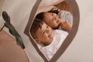 Cute little children lying in toy wigwam at home