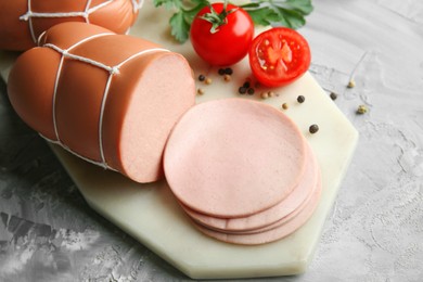 Photo of Delicious boiled sausage with tomatoes, parsley and spices on grey textured table