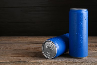 Photo of Energy drinks in wet cans on wooden table, space for text