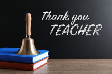 School bell and books on wooden table near blackboard with phrase Thank You Teacher