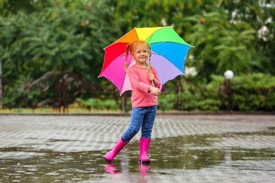 Cute little girl with bright umbrella under rain on street
