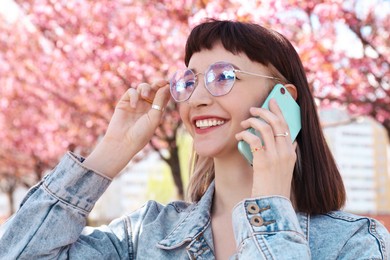 Photo of Beautiful young woman talking on phone in park with blossoming sakura trees