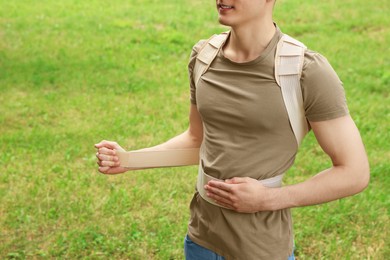 Closeup view of man with orthopedic corset on green grass outdoors, space for text