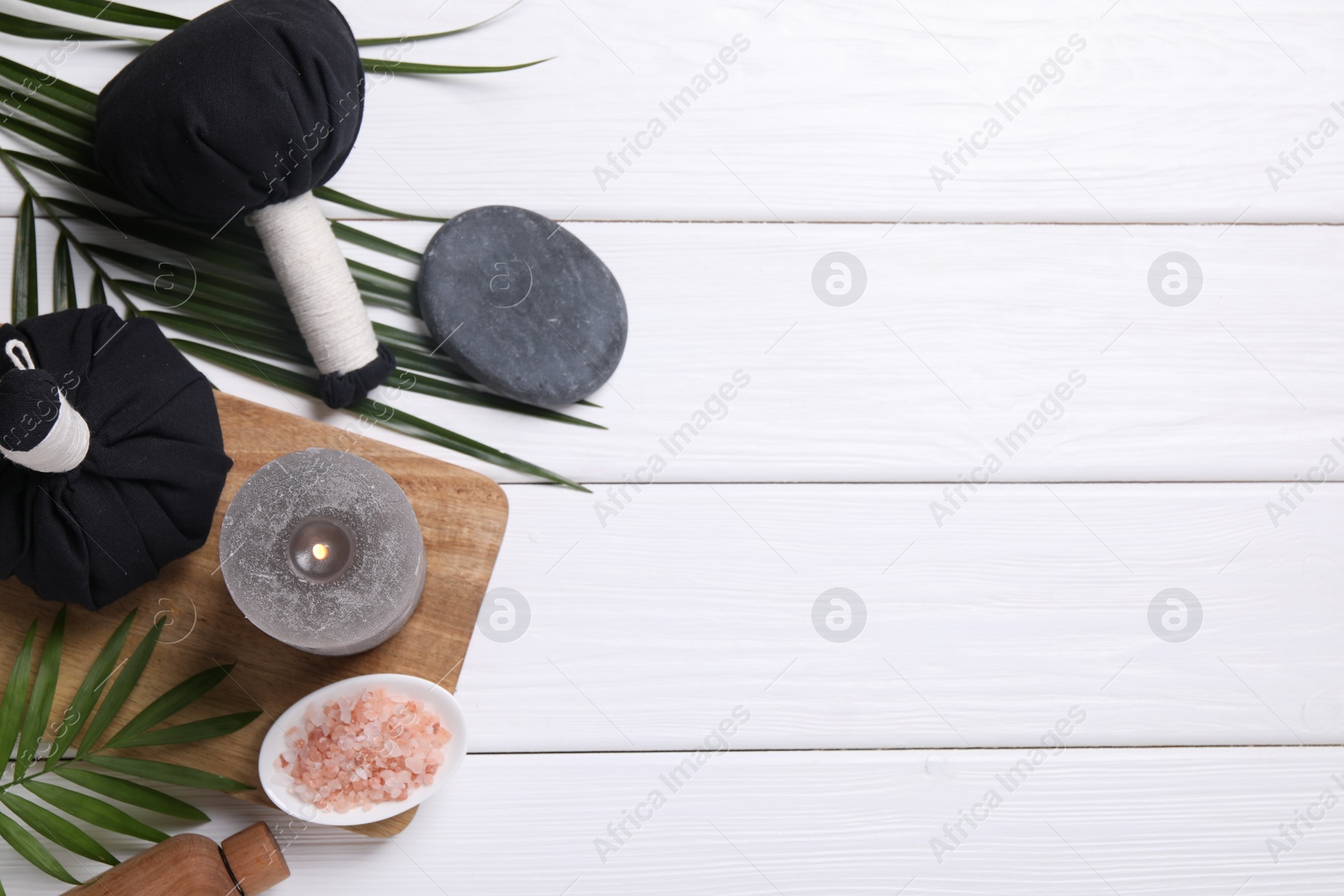 Photo of Beautiful spa composition with herbal massage bags, burning candle and leaves on white wooden table, flat lay. Space for text