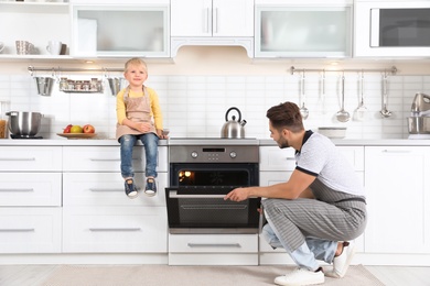 Photo of Young man and his son baking something in oven at home