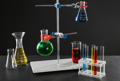Photo of Retort stand and laboratory glassware with liquids on table against black background