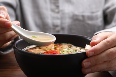 Photo of Woman eating delicious ramen with spoon at table, closeup. Noodle soup