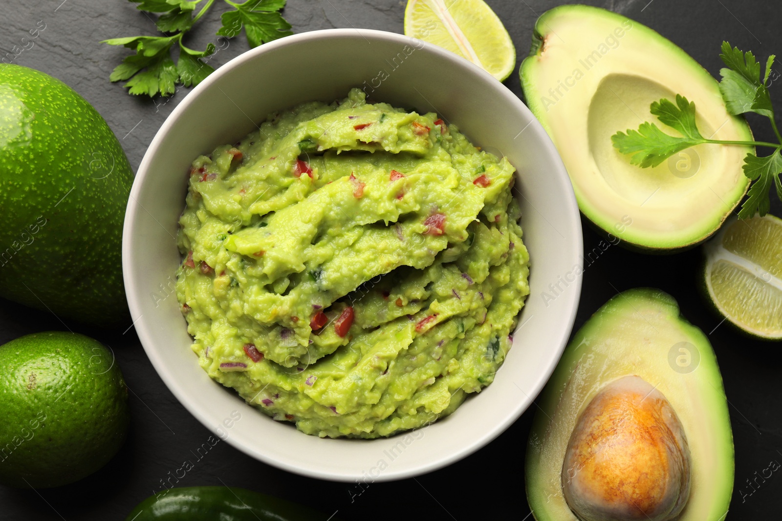 Photo of Delicious guacamole, fresh avocado and parsley on dark grey table, flat lay