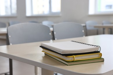 Stack of notebooks on wooden desk in empty classroom