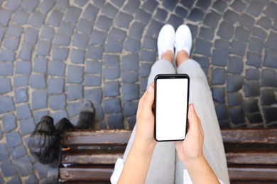 Photo of Closeup of woman with smartphone sitting on bench outdoors, top view