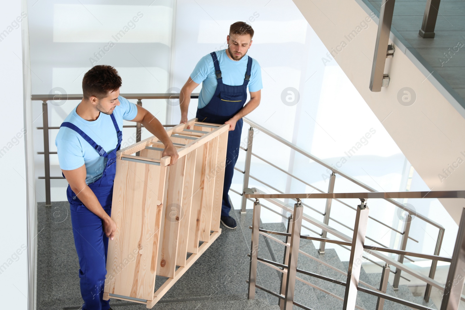 Photo of Professional workers carrying wooden rack on stairs in office. Moving service