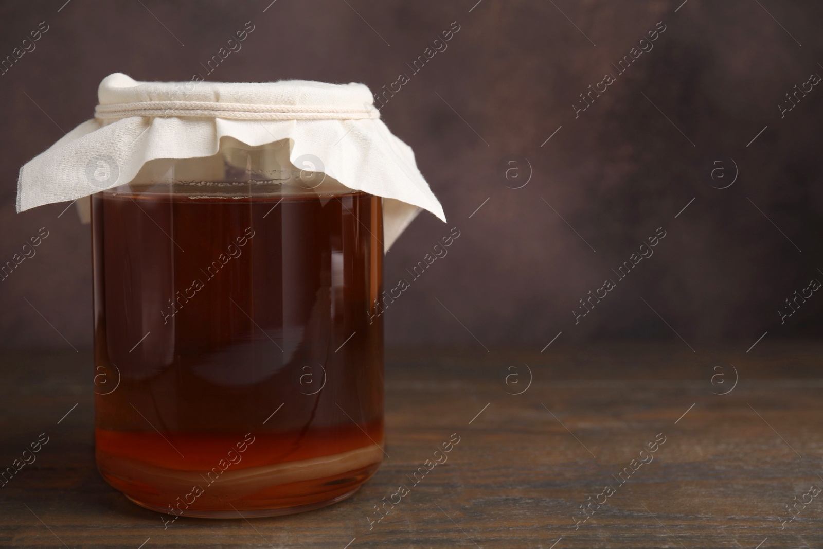 Photo of Tasty kombucha in glass jar on wooden table, space for text