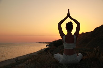 Photo of Woman meditating near sea at sunset, back view. Space for text