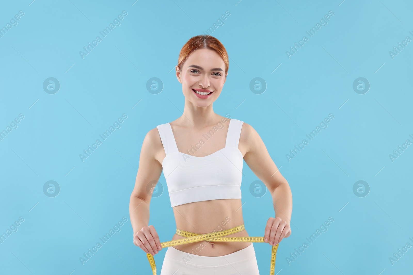 Photo of Slim woman measuring waist with tape on light blue background. Weight loss