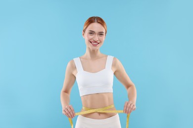 Photo of Slim woman measuring waist with tape on light blue background. Weight loss
