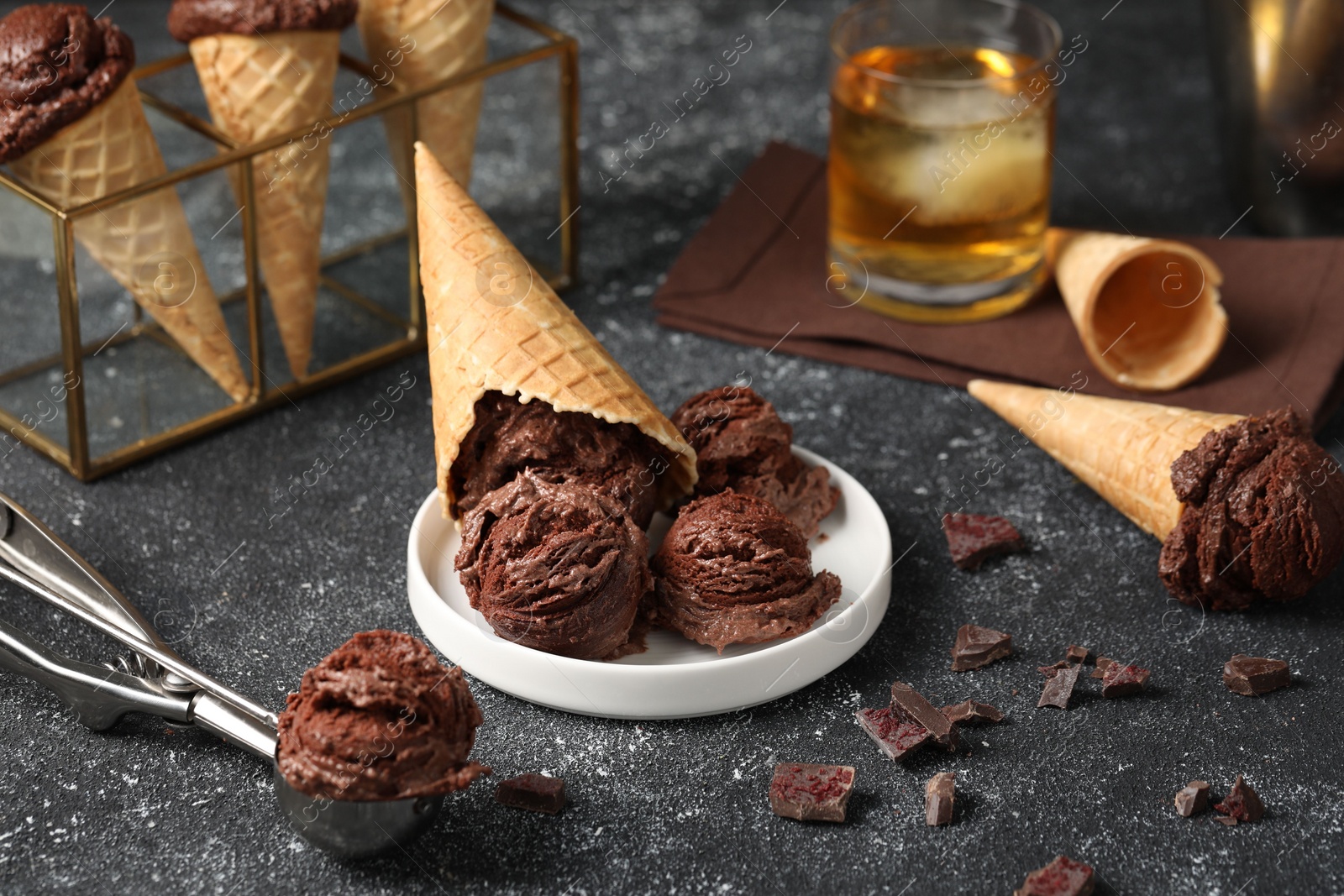 Photo of Tasty ice cream scoops, chocolate crumbs and waffle cones on dark textured table, closeup