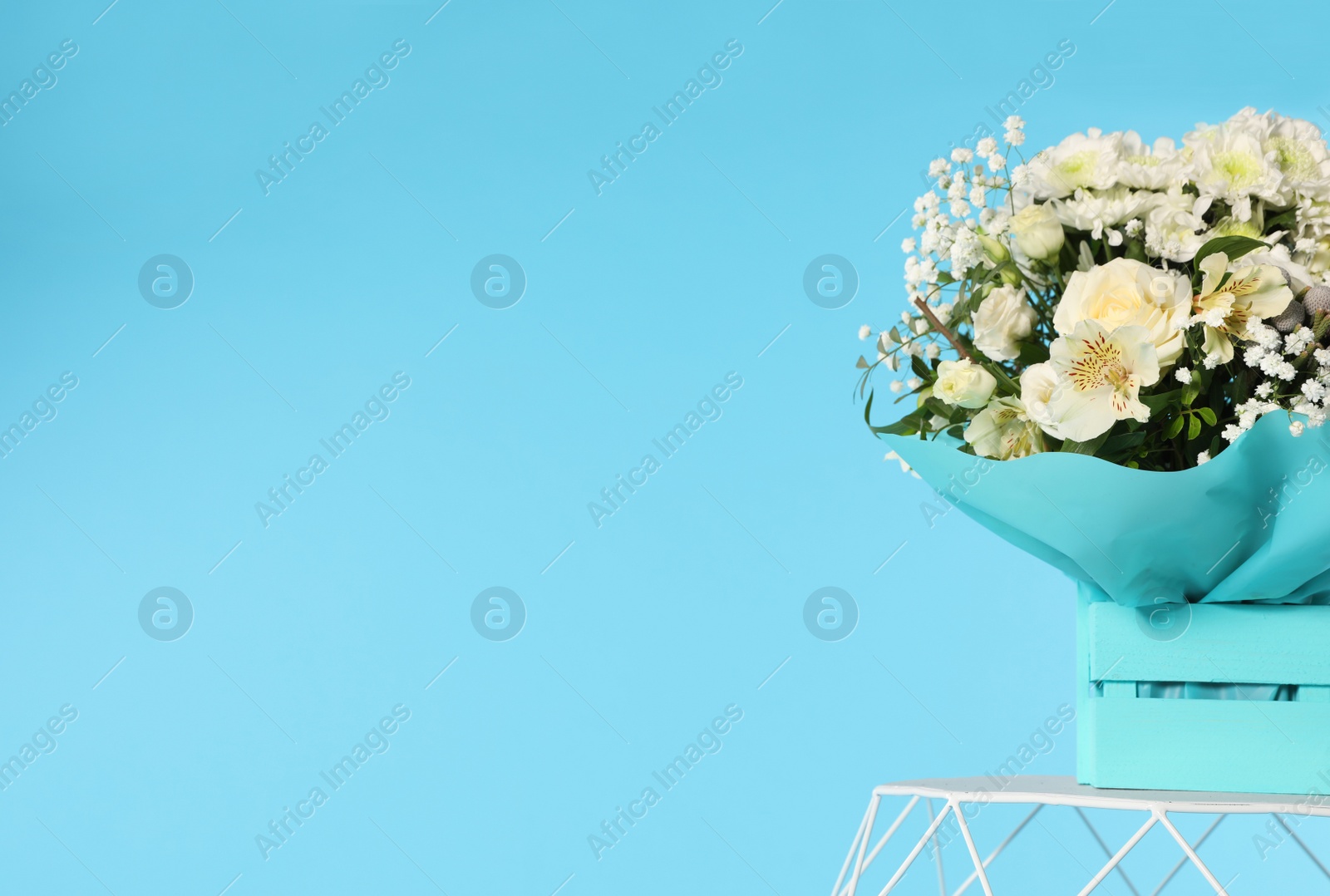 Photo of Beautiful bouquet of flowers in decorative crate on table against color background. Space for text