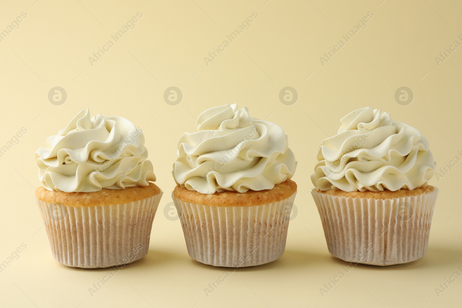 Photo of Tasty vanilla cupcakes with cream on pale yellow background