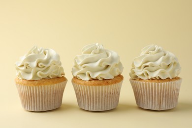 Tasty vanilla cupcakes with cream on pale yellow background