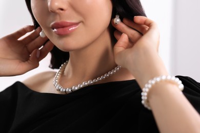 Young woman wearing elegant pearl jewelry indoors, closeup