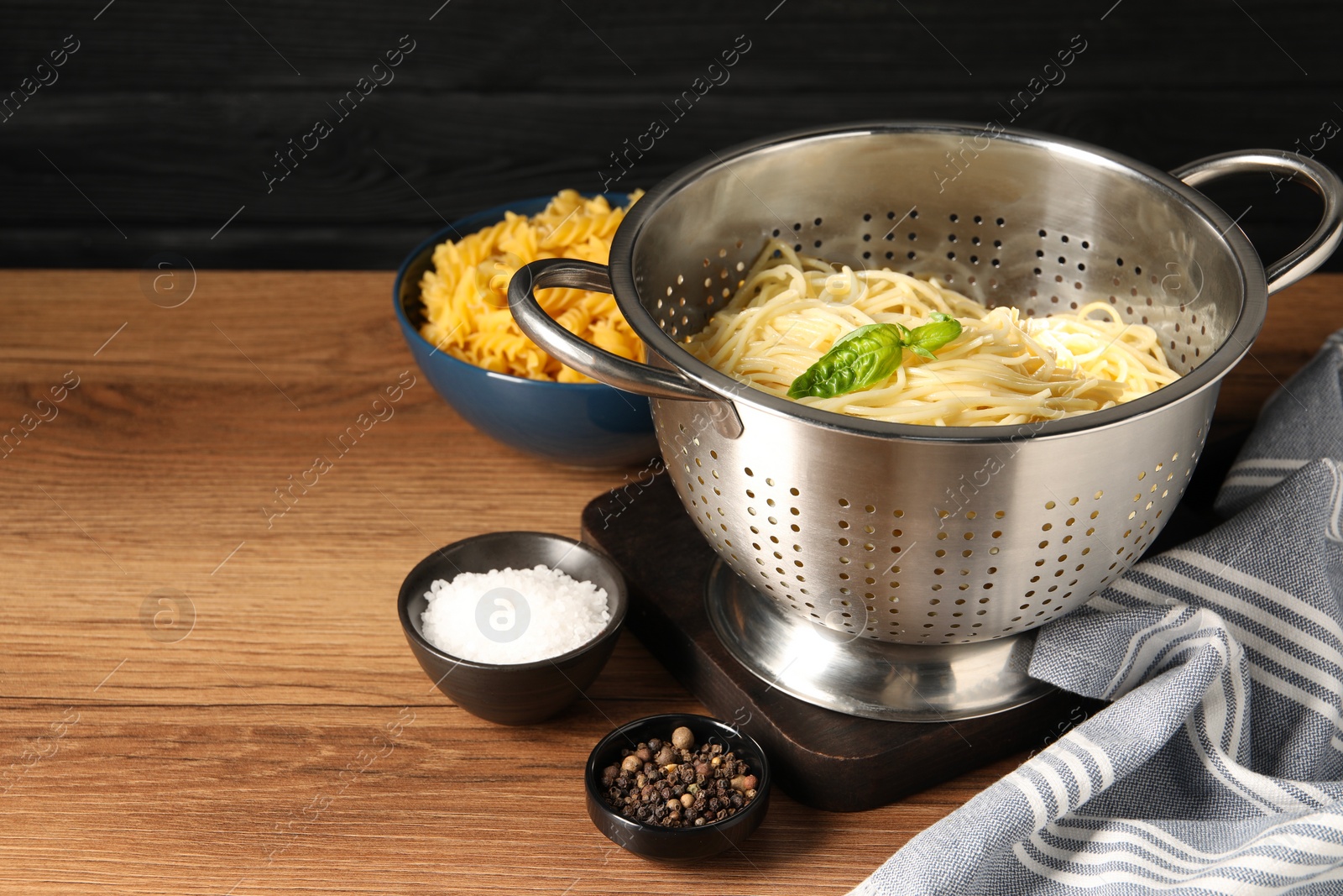 Photo of Cooked pasta in metal colander and spices on wooden table. Space for text