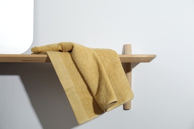 Photo of Yellow terry towel on wooden shelf near white wall