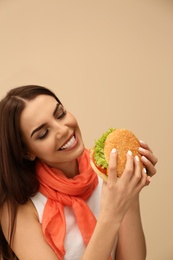 Photo of Young woman eating tasty burger on color background. Space for text