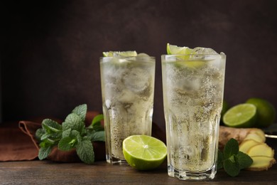 Photo of Glasses of tasty ginger ale with ice cubes and ingredients on wooden table, space for text