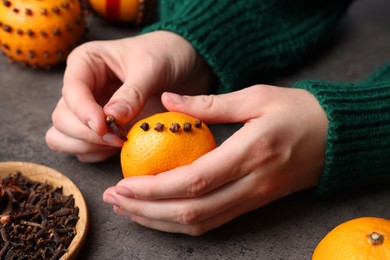 Photo of Woman decorating fresh tangerine with cloves at grey table, closeup
