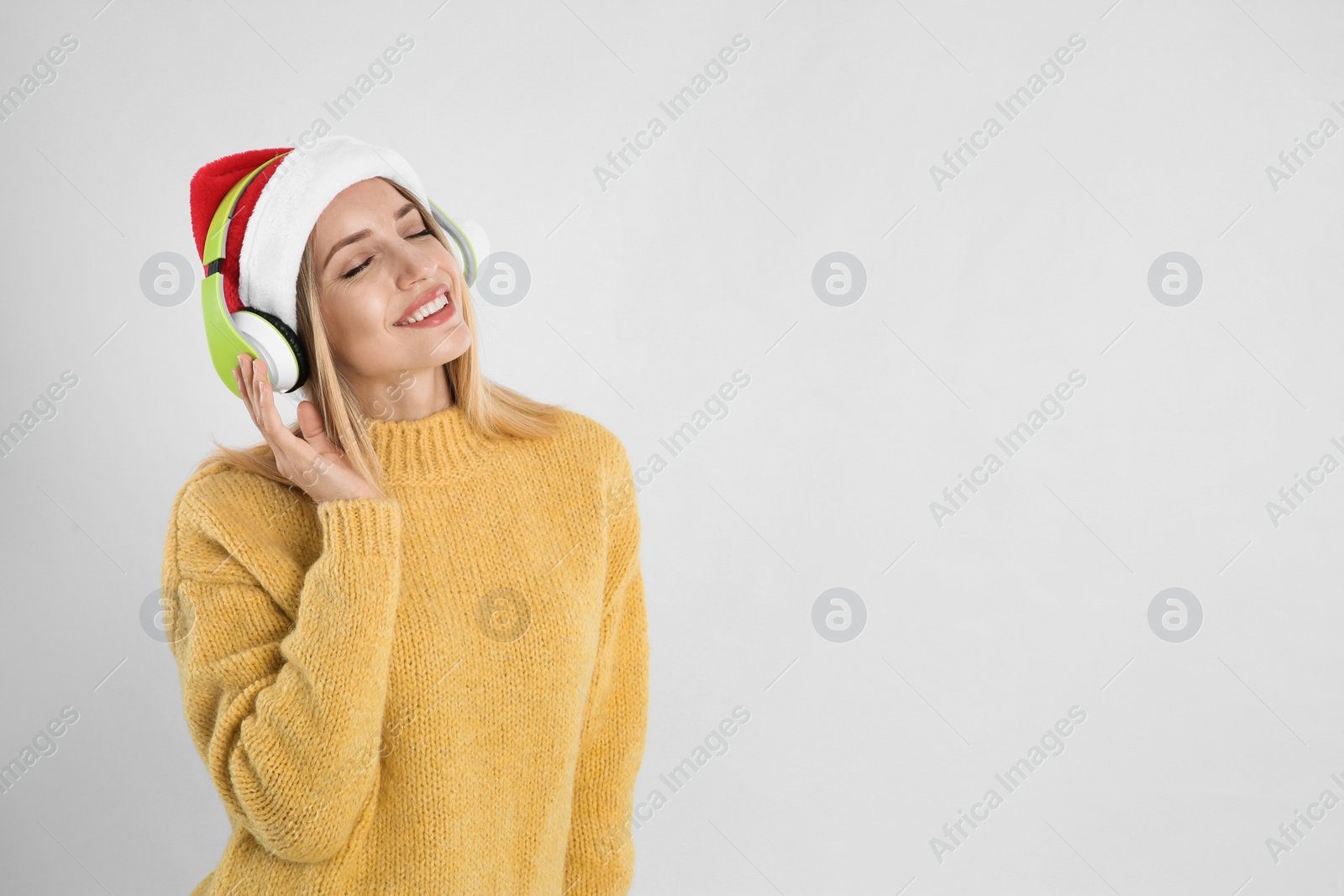 Photo of Happy woman with headphones on light grey background, space for text. Christmas music