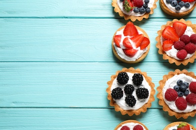 Photo of Many different berry tarts on blue wooden table, flat lay with space for text. Delicious pastries