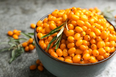 Fresh ripe sea buckthorn in bowl on grey table, closeup