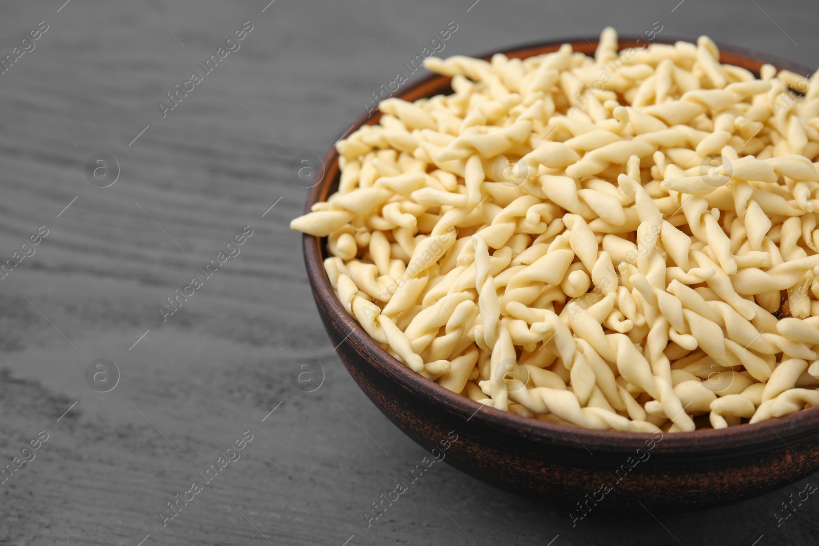 Photo of Uncooked trofie pasta in bowl on grey wooden table, closeup. Space for text