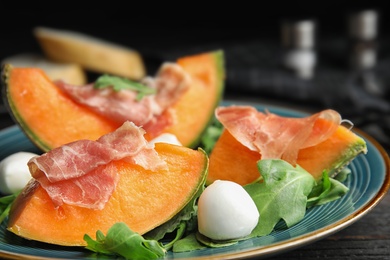 Photo of Fresh melon with prosciutto, mozzarella and arugula on plate, closeup