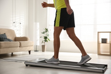 Photo of Sporty man training on walking treadmill at home, closeup