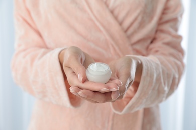 Photo of Young woman holding jar of cream at home, closeup