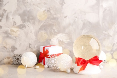 Image of Beautiful Christmas snow globe with red bow, gift box and decor on light table, bokeh effect. Space for text