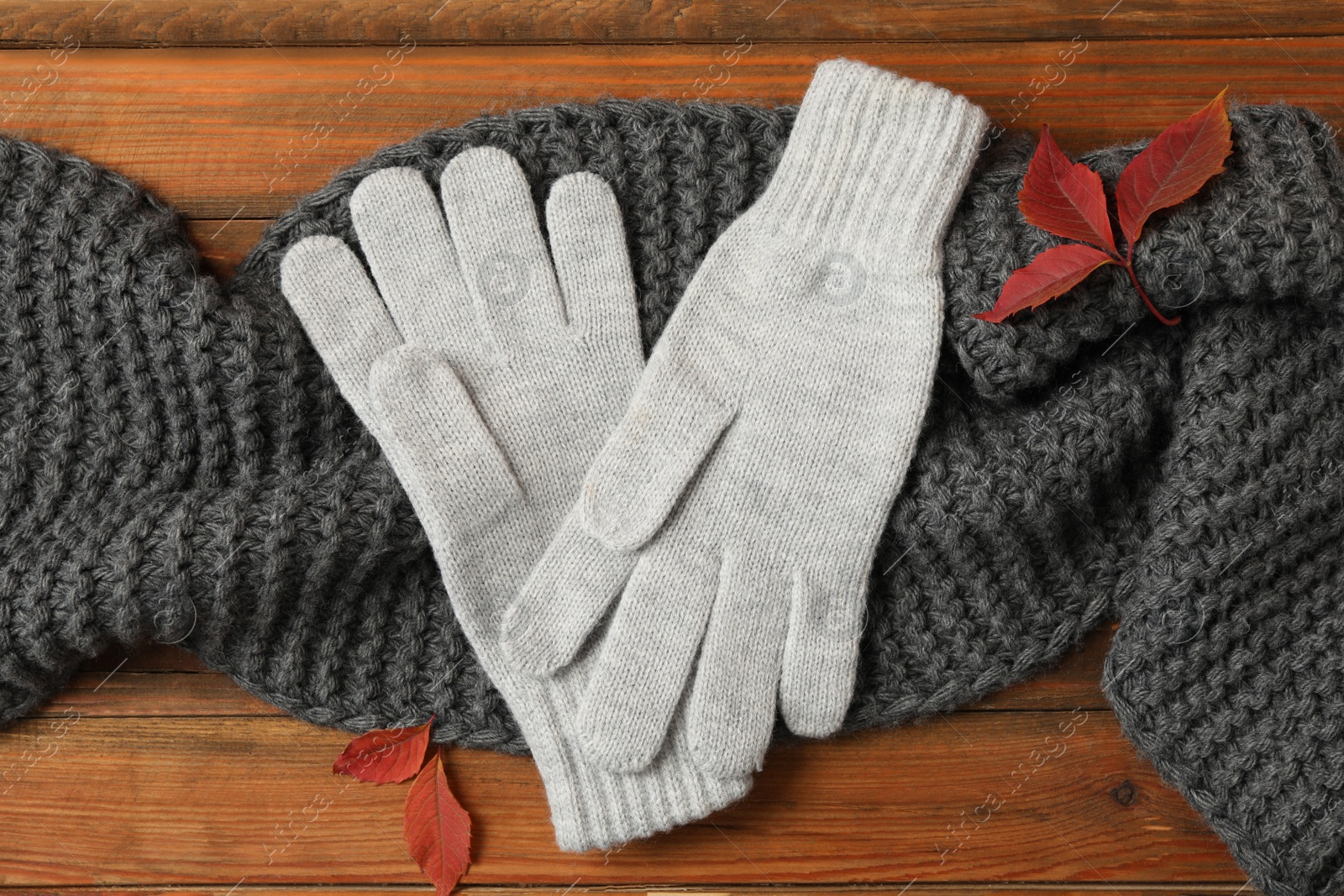 Photo of Stylish woolen gloves, scarf and dry leaves on wooden table, flat lay