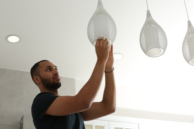 Young man repairing ceiling lamp indoors, space for text