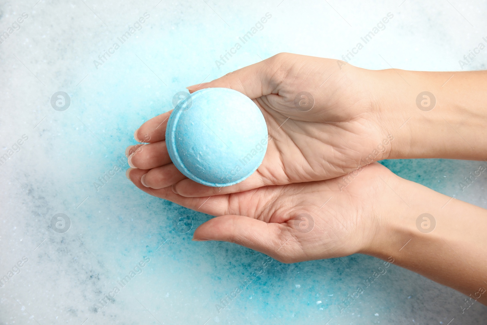 Photo of Woman holding color bath bomb over foam, top view