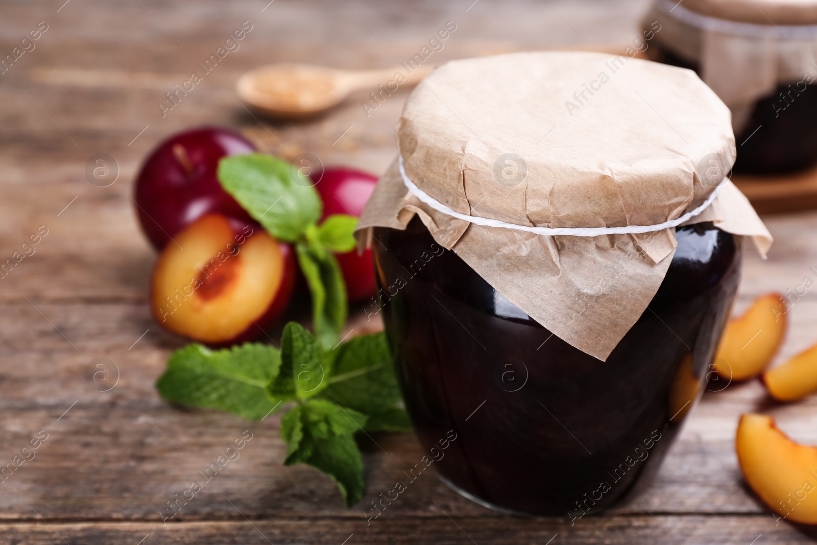 Photo of Glass jar of pickled plums on wooden table, closeup. Space for text