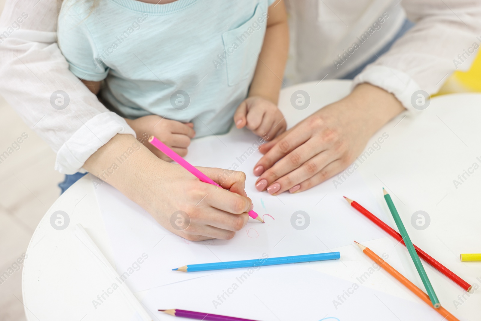 Photo of Mother and her little daughter drawing with colorful pencils at white table, closeup