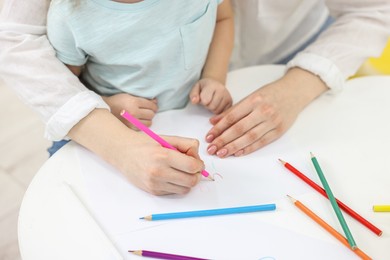 Photo of Mother and her little daughter drawing with colorful pencils at white table, closeup